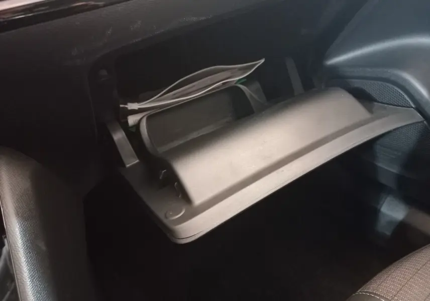 Gros plan sur la boîte à gants ouverte noire du Peugeot 2008 orange, avec des papiers et câbles visibles à l'intérieur.