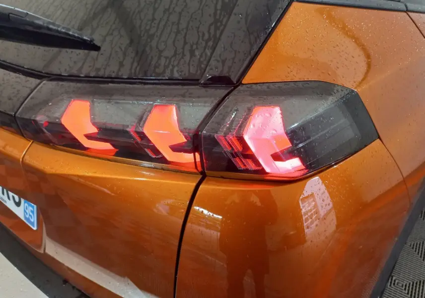 Gros plan sur le feu arrière gauche allumé d’un Peugeot 2008 orange 2021 sous la pluie.