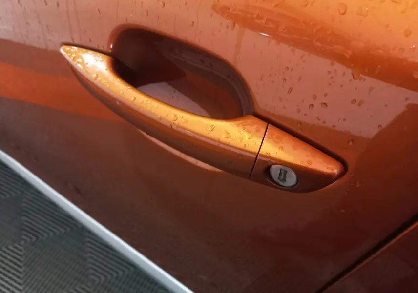 Poignée de porte avant droite orange métallisé de Peugeot 2008 BlueHDi 110 S&S Allure Business 2021 avec gouttes d'eau visibles.