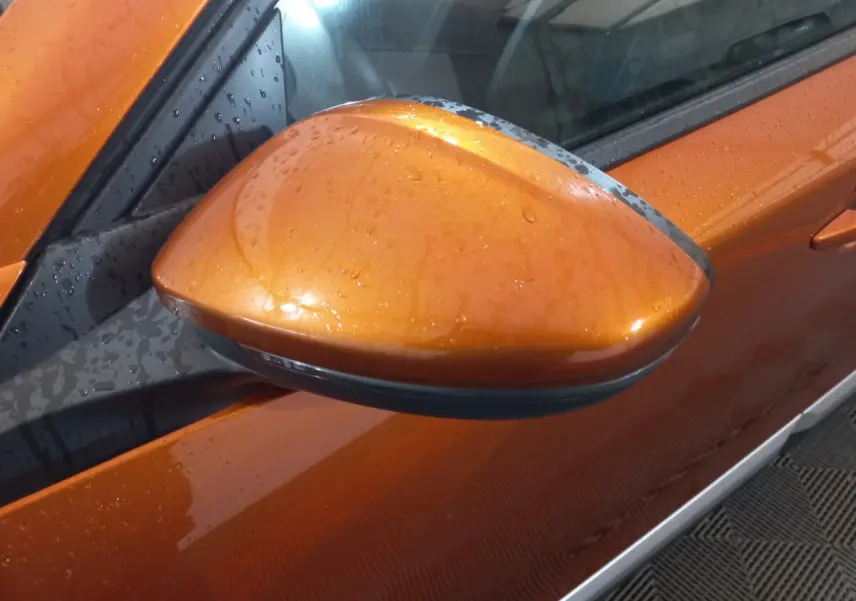 Rétroviseur côté gauche orange brillant de la Peugeot 2008 BlueHDi 110 S&S Allure Business 2021 avec gouttes d'eau visibles.