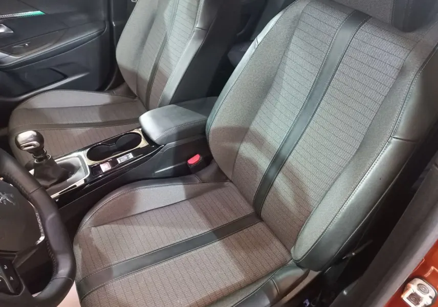 Vue intérieure côté conducteur du Peugeot 2008 orange 2021, montrant sièges tissu et cuir avec console centrale et levier de vitesse manuel.