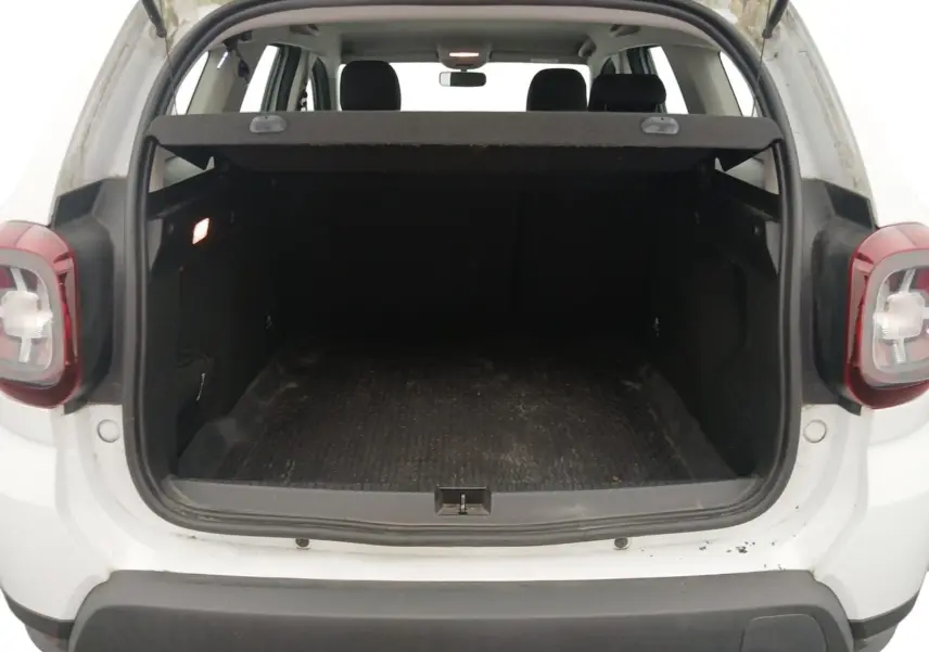 Coffre ouvert vu de l'arrière d'un Dacia Duster blanc 2021, montrant l'espace de chargement et les feux arrière.
