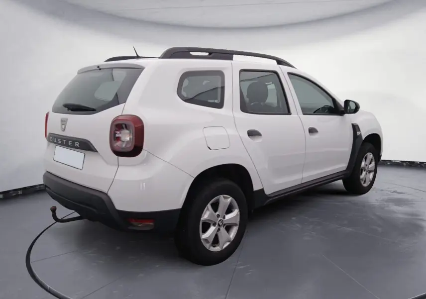 Vue 3/4 arrière droite d'un Dacia Duster blanc 2021 avec barres de toit noires et feux arrière LED.