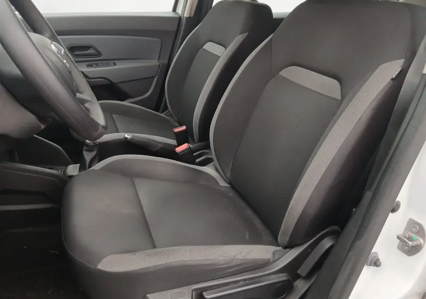 Vue intérieure côté conducteur du Dacia Duster blanc 2021, sièges tissu noir avec détails gris et volant visible.
