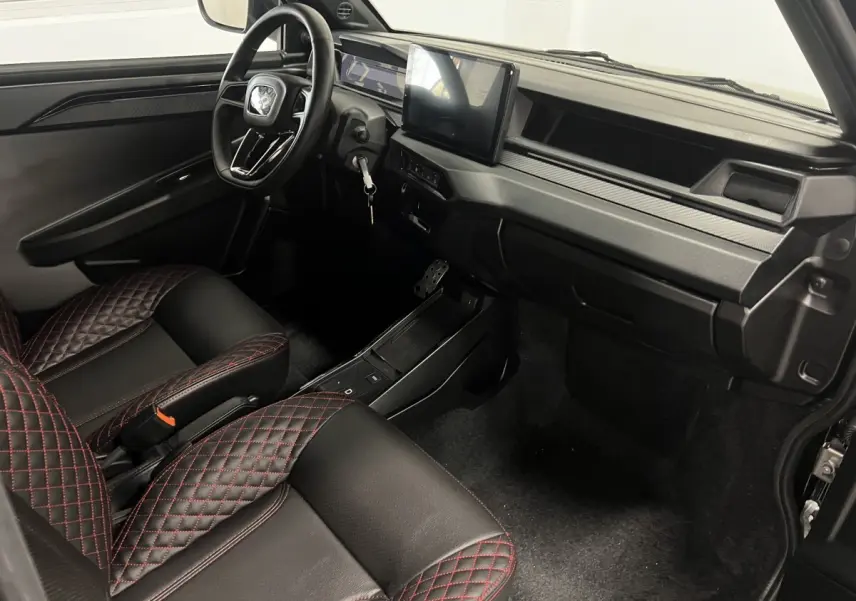 Intérieur avant droit de la LIGIER JS50 0.5 REVO D+ ULTIMATE 2026, sièges noirs avec surpiqûres rouges et écran tactile central.