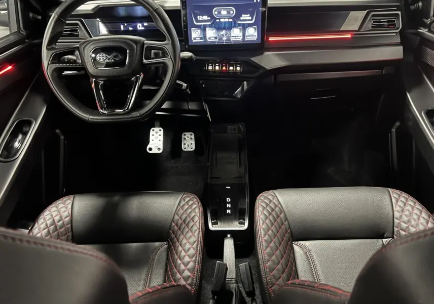 Vue intérieure avant du tableau de bord noir de la Ligier JS50 Ultimate avec écran tactile et sièges cuir surpiqués rouges.
