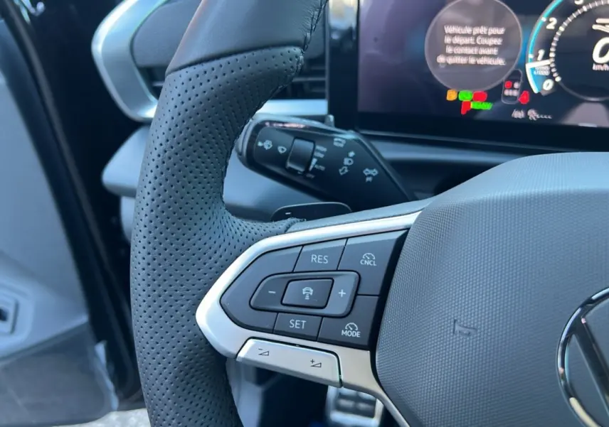 Gros plan sur le volant cuir noir perforé du Volkswagen T-Roc 2026 avec commandes multifonctions et affichage digital en arrière-plan.