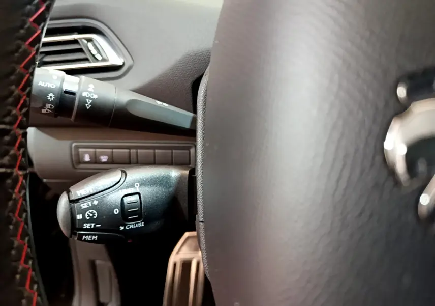 Gros plan sur la commande de régulateur de vitesse à gauche du volant cuir noir d'une Peugeot 308 gris foncé.