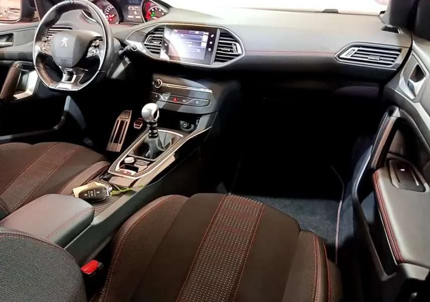 Intérieur avant droit de Peugeot 308 GT Line 2016, sièges noirs avec surpiqûres rouges et écran tactile central.