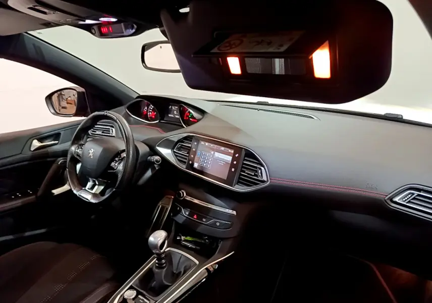 Vue intérieure côté conducteur du tableau de bord et volant cuir d'une Peugeot 308 gris foncé avec écran tactile central allumé.