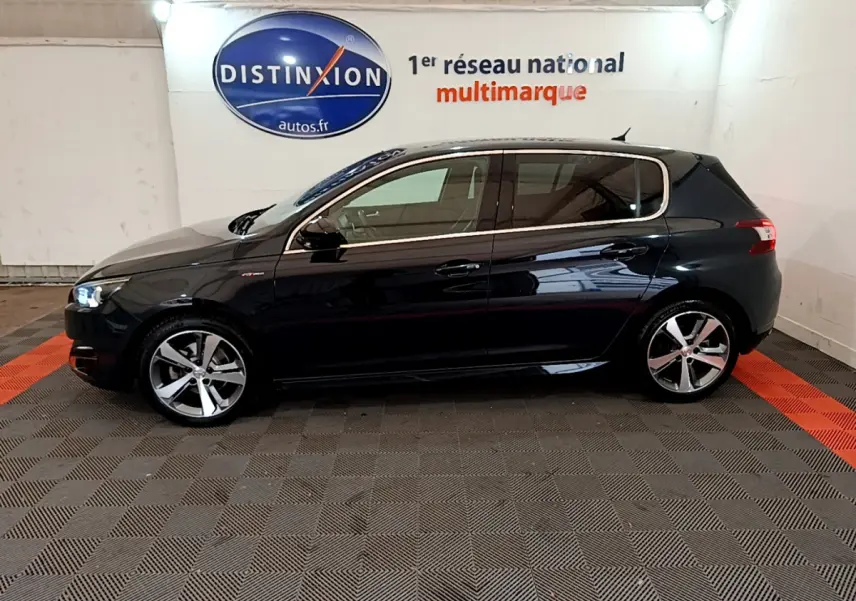 Profil côté gauche d'une Peugeot 308 gris foncé 2016 GT Line avec jantes alliage et feux allumés en intérieur showroom.