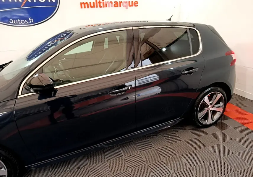 Profil côté gauche d'une Peugeot 308 gris foncé, avec jantes alliage et vitres teintées en intérieur showroom.