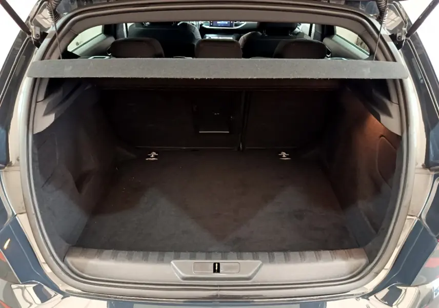 Coffre ouvert vu de l'arrière d'une Peugeot 308 gris foncé, montrant l'espace de chargement et la tablette cache-bagages.