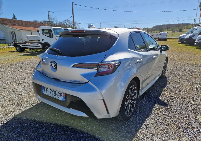 Vue 3/4 arrière droite d'une Toyota Corolla hybride gris clair métal avec vitres teintées et jantes alliage.