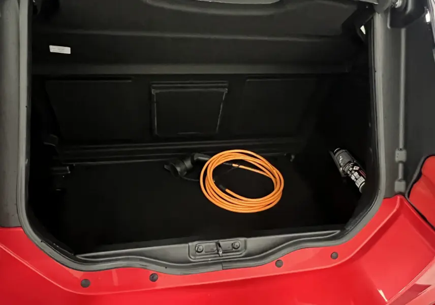 Vue plongeante sur le coffre ouvert rouge d'une LIGIER JS50 BEV 8KWH ELITE avec câble de charge orange à l'intérieur.