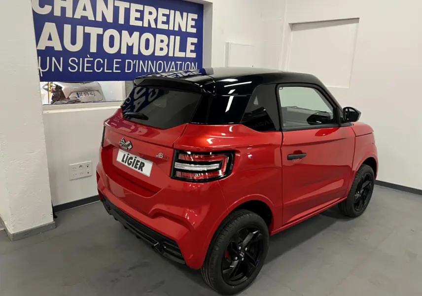 Vue 3/4 arrière droite d'une Ligier JS50 BEV 8KWH Elite rouge avec toit noir et jantes alu noires.