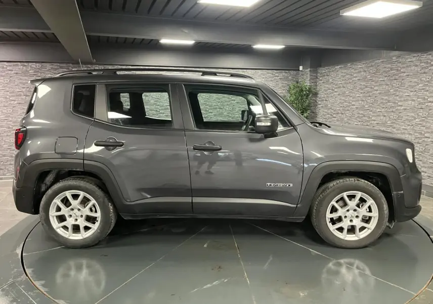 Profil côté gauche d'un Jeep Renegade gris métallisé 2024 avec jantes alliage 17 pouces et barres de toit noires.