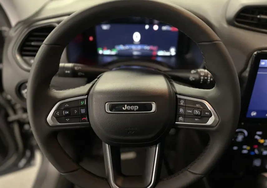 Volant noir Jeep Renegade 2024 avec commandes intégrées, tableau de bord numérique et écran tactile visible en arrière-plan.