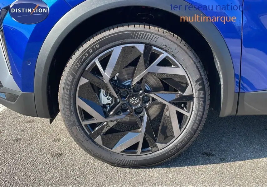 Gros plan sur la roue avant gauche du Renault Captur bleu Iron Metal avec jante noire au design géométrique.