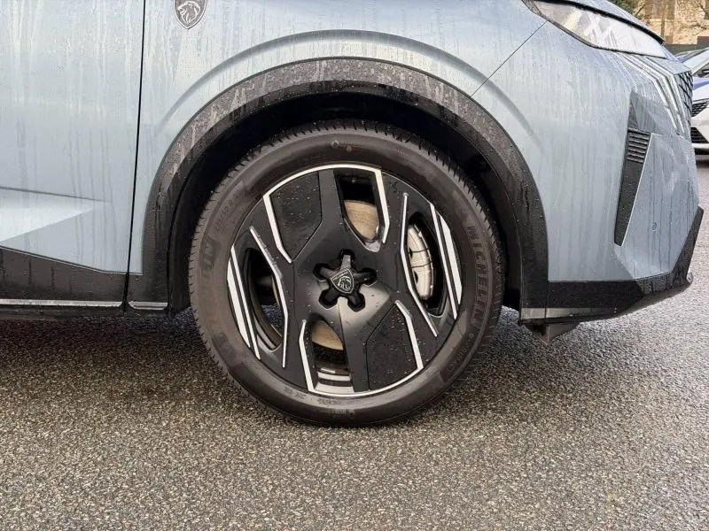 Gros plan sur la roue avant gauche du Peugeot 3008 électrique bleu avec jante alu noire et détails argentés.