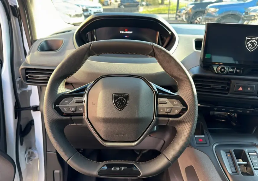 Vue intérieure centrée sur le volant cuir multifonctions du Peugeot Rifter GT Plus 2025, avec écran tactile et tableau de bord numérique.