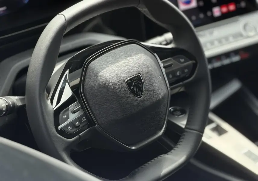 Gros plan sur le volant cuir noir de la Peugeot 308 SW 2025 avec commandes intégrées et logo lion central.