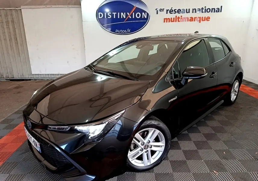 Toyota Corolla hybride noire vue en 3/4 avant droit dans un showroom avec jantes argentées et logo Distinxion en arrière-plan