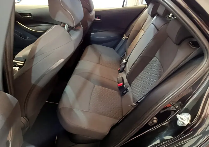 Vue intérieure côté gauche montrant la banquette arrière noire de la Toyota Corolla Hybride 2021 avec sièges tissu et ceintures visibles.