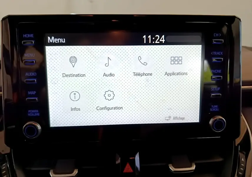 Écran tactile central allumé de la Toyota Corolla hybride 2021, avec menu blanc et boutons noirs autour.