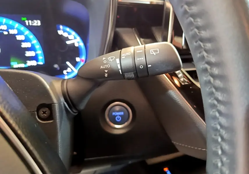 Gros plan sur la manette d’essuie-glace à gauche du volant cuir noir, avec bouton démarrage bleu illuminé en arrière-plan.