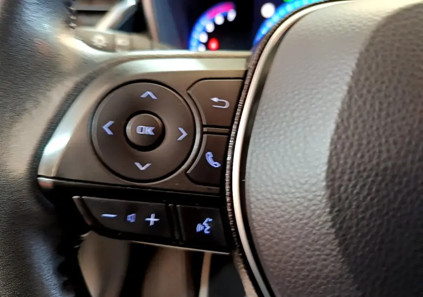 Gros plan sur les commandes gauche du volant en cuir noir de la Toyota Corolla hybride 2021 avec boutons rétroéclairés.