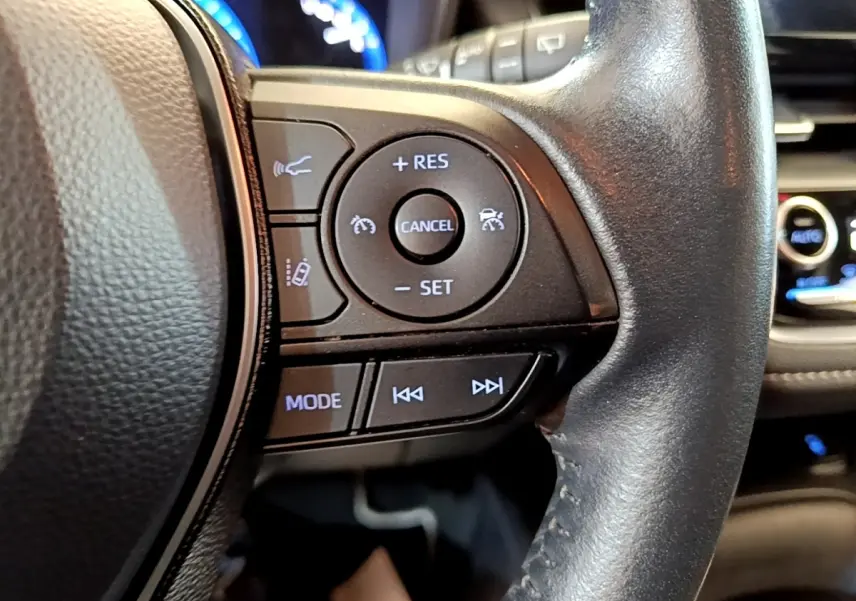 Gros plan sur les commandes du volant cuir à droite de la Toyota Corolla hybride noire, avec affichage numérique en arrière-plan.