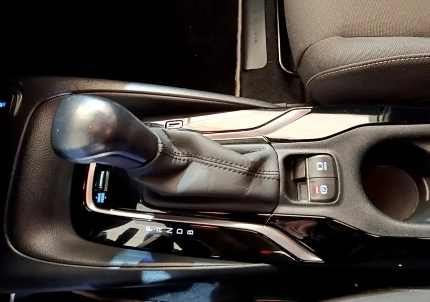 Gros plan sur la console centrale noire de la Toyota Corolla hybride 2021, avec levier de vitesse automatique et commandes électroniques.