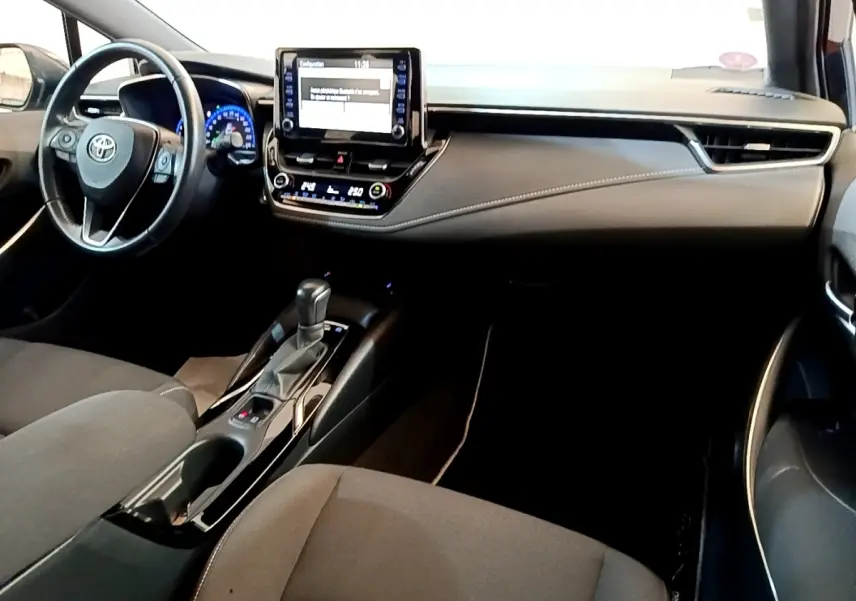 Intérieur noir de la Toyota Corolla Hybride 2021, vue du tableau de bord et console centrale avec écran tactile et volant cuir.