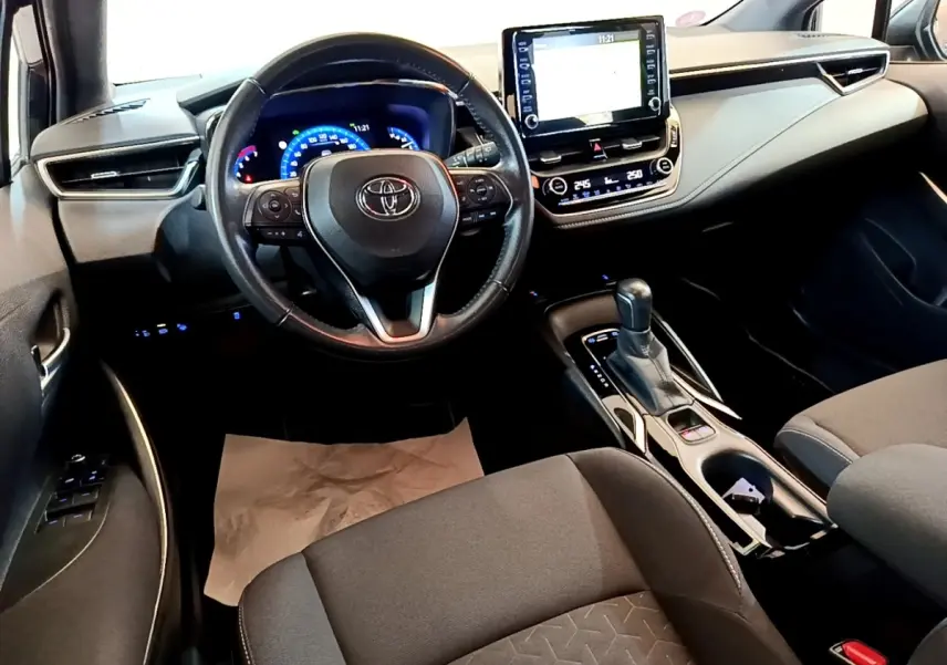 Intérieur noir de la Toyota Corolla Hybride 2021, vue du poste de conduite avec écran tactile central et volant cuir.