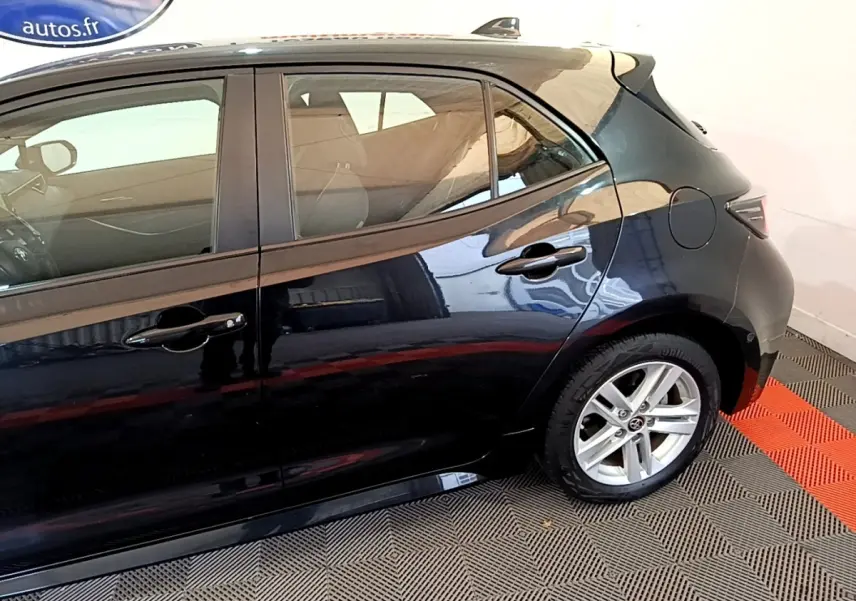 Profil côté droit de la Toyota Corolla hybride noire 2021, mettant en valeur la jante alliage et les poignées de porte chromées.