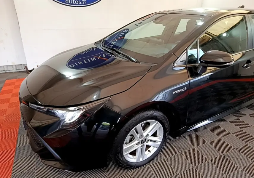 Toyota Corolla hybride noire vue de 3/4 avant droit, mettant en valeur ses phares LED et la mention Hybrid sur la portière.