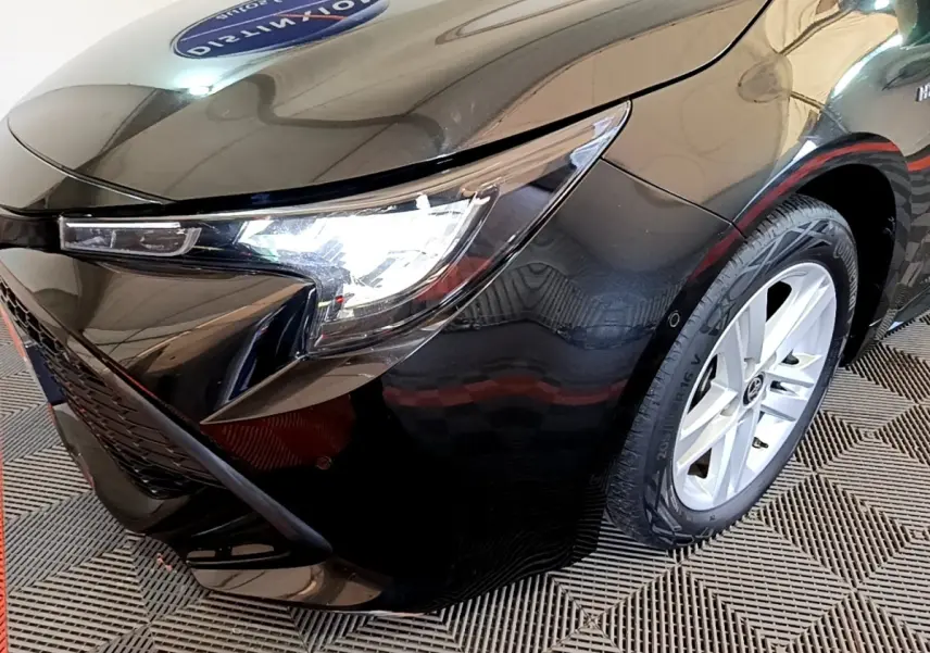 Gros plan sur l'avant droit noir brillant de la Toyota Corolla hybride 2021 avec phare LED allumé et jante argentée.