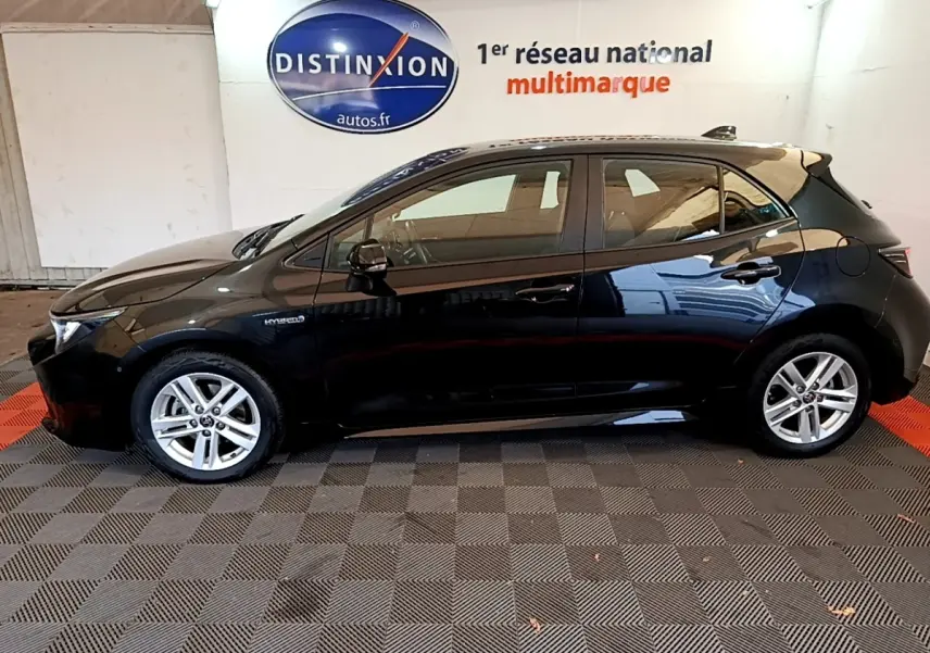 Profil côté gauche d'une Toyota Corolla hybride noire 2021, avec jantes alliage et badge Hybrid visible sur l'aile avant.
