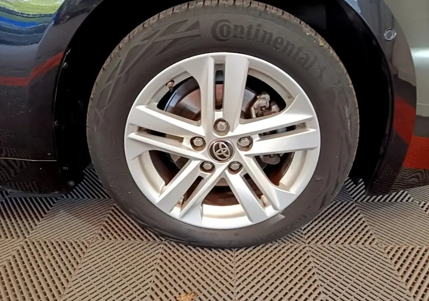 Gros plan sur la roue avant gauche noire de la Toyota Corolla hybride, avec jante alliage argentée et logo Toyota central.