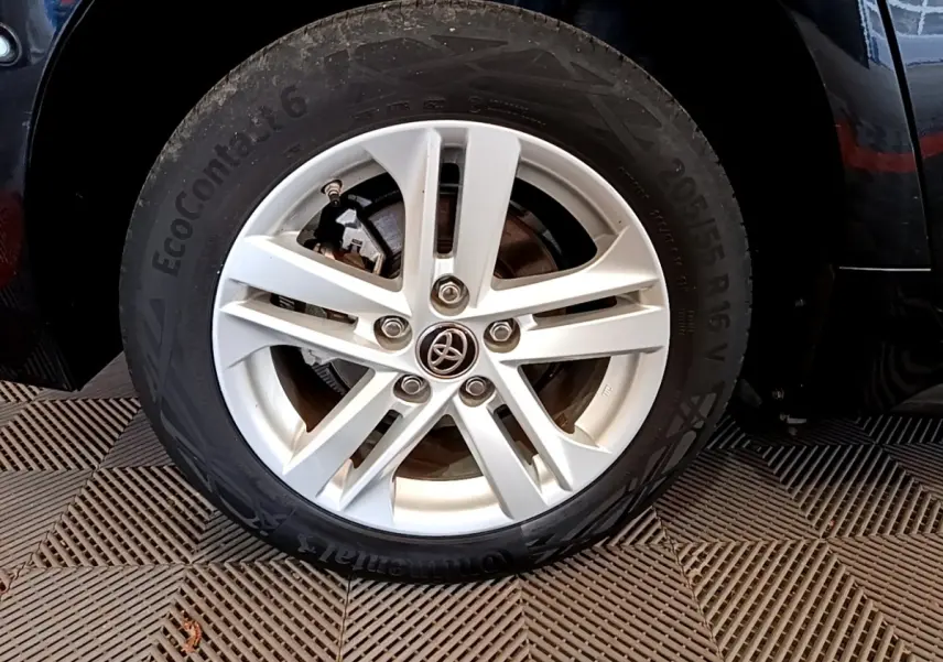 Gros plan sur la roue avant droite d'une Toyota Corolla noire, jante alliage argentée avec logo Toyota central.