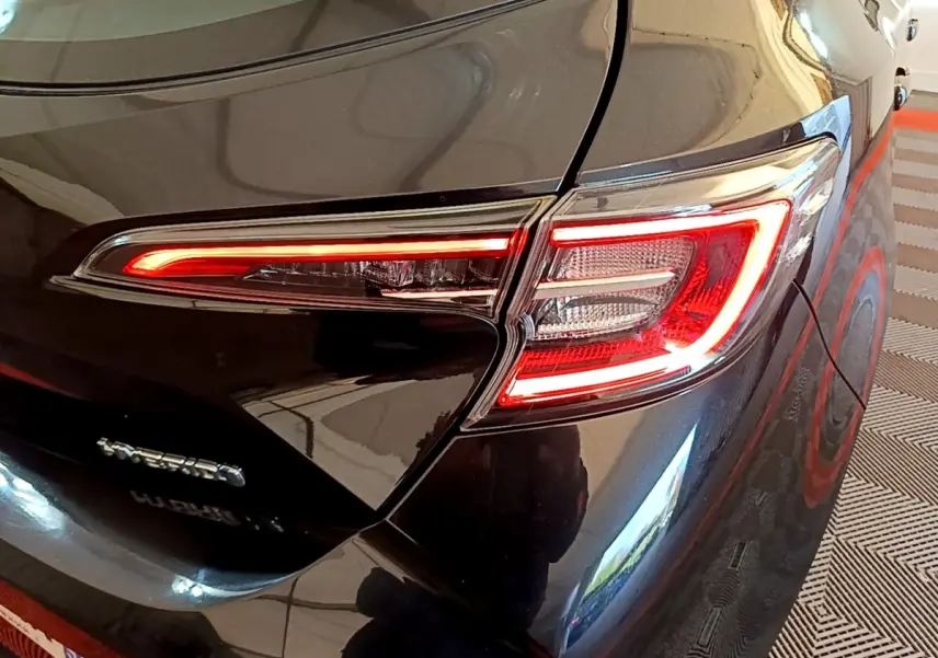 Feu arrière droit allumé sur une Toyota Corolla hybride noire, vue rapprochée du coin arrière du véhicule.