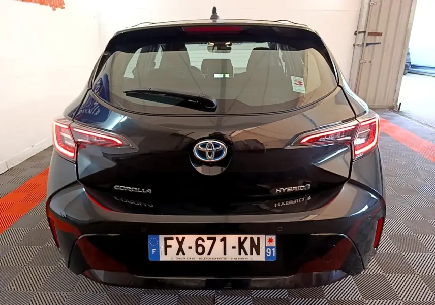 Vue arrière d'une Toyota Corolla hybride noire, avec feux LED allumés et plaque d'immatriculation française visible.