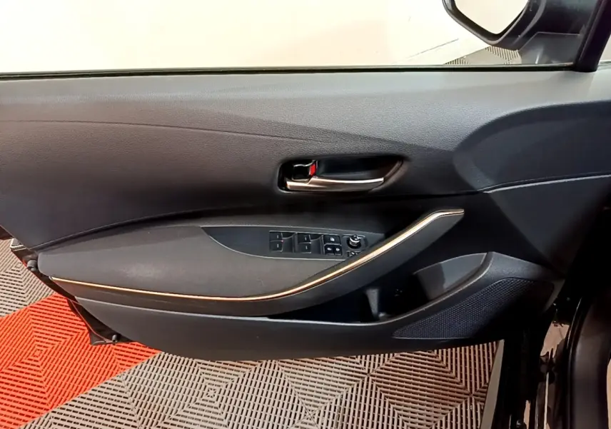 Vue intérieure côté gauche de la porte avant noire de la Toyota Corolla hybride avec commandes de vitres et poignée chromée.