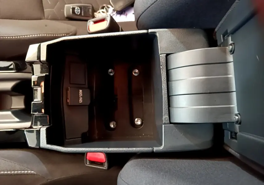 Vue plongeante sur le rangement central noir ouvert de la Toyota Corolla hybride 2021, montrant prise 12V et console entre sièges.