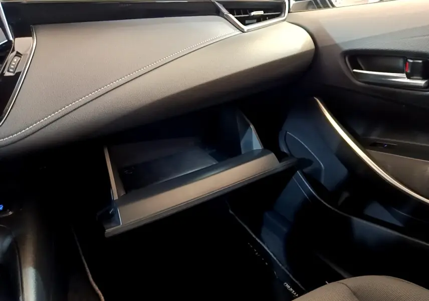 Intérieur côté passager de la Toyota Corolla hybride 2021, boîte à gants ouverte et tableau de bord noir avec surpiqûres blanches.