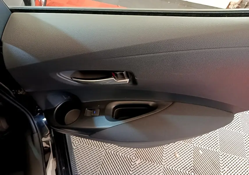 Intérieur côté gauche de la porte noire d'une Toyota Corolla Hybride 2021 avec poignée argentée et commande de vitre.