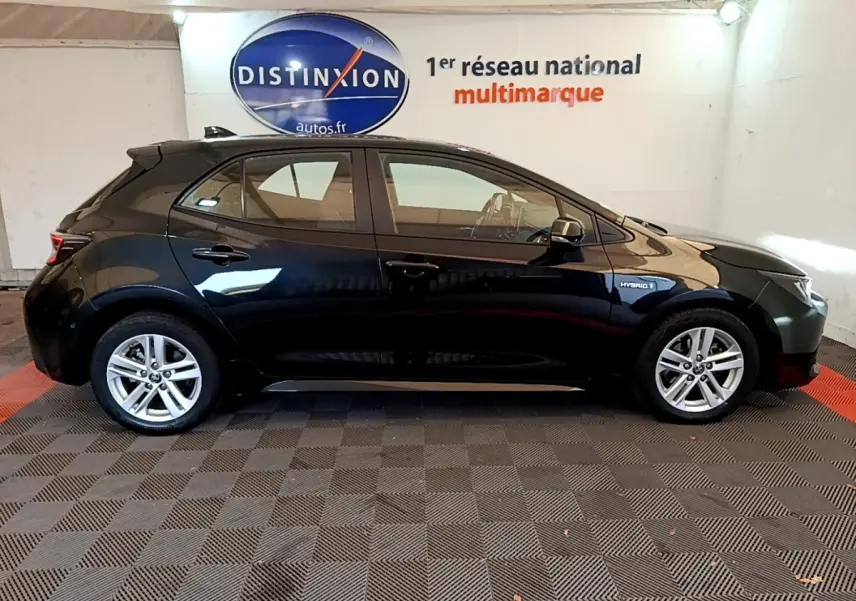 Profil côté gauche d'une Toyota Corolla hybride noire 2021 avec jantes alliage et badge Hybrid visible sur l'aile avant.