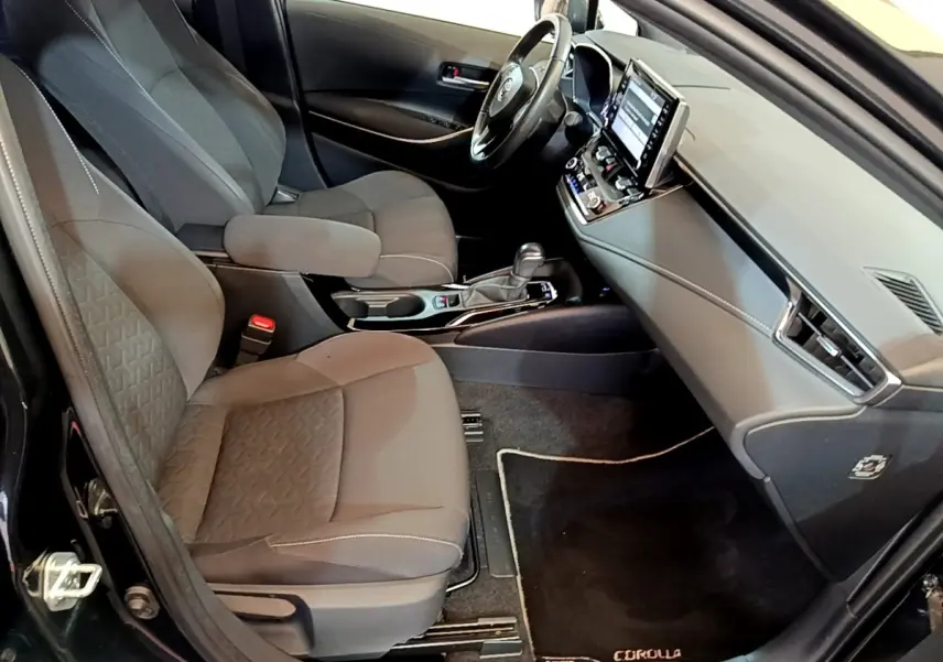 Intérieur noir vu côté passager avant de la Toyota Corolla hybride 2021 avec tableau de bord moderne et écran tactile.