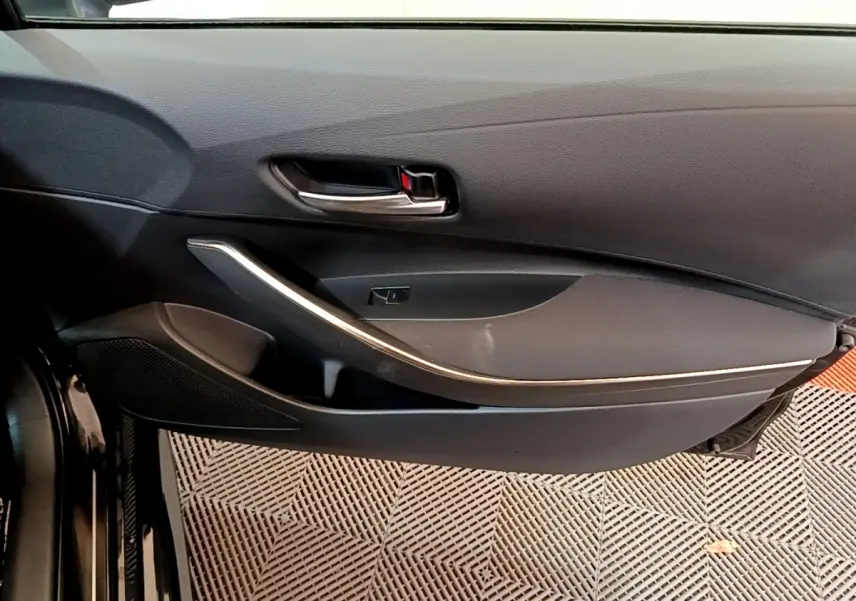 Gros plan sur la porte intérieure côté conducteur noire de la Toyota Corolla hybride 2021 avec poignée chromée et garniture argentée.